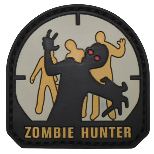 A circular tactical patch with a black border and the words 'ZOMBIE HUNTER' at the bottom. The design shows a black zombie figure in front of three tan figures on a light gray background, with red eyes.